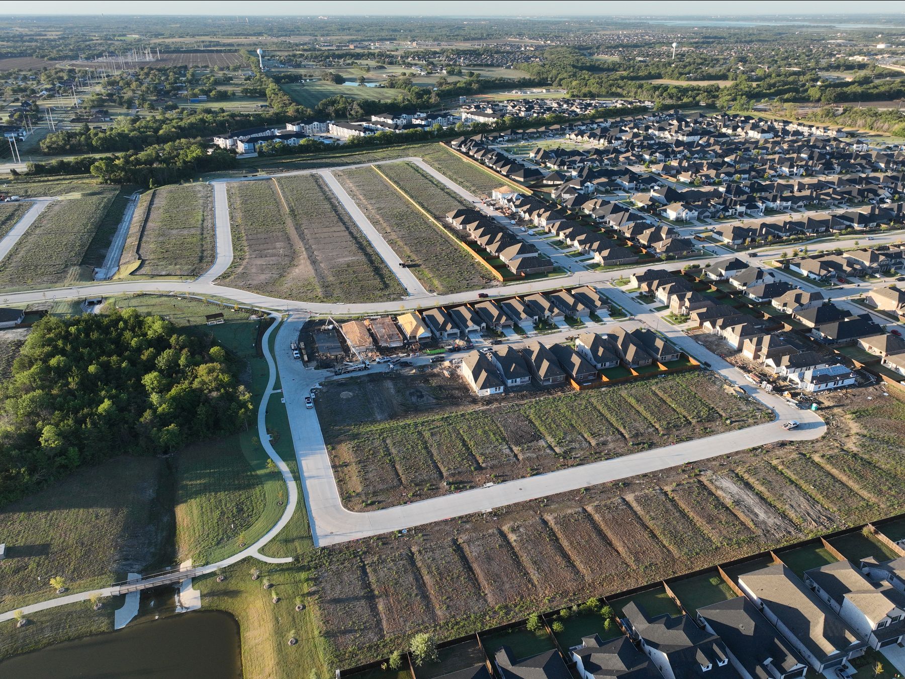 Aerial view of new homes beside rows of finished homesites, a walking trail and a pond at Elevon Section 1, Phase 4 in Lavon, Texas